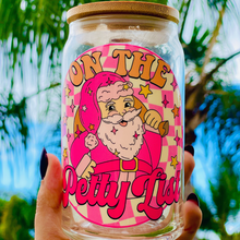 Load image into Gallery viewer, A 16 oz glass cup featuring a festive pink Santa design with the phrase &quot;On The Petty List.&quot; Includes a bamboo lid and reusable glass straw, perfect for cold drinks. BPA-free and handwash only.
