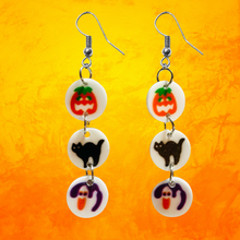 Load image into Gallery viewer, Earrings featuring mini replicas of Pillsbury Halloween sugar cookies, including jack-o&#39;-lanterns, black cats, and ghosts, dangling from hooks against an orange background. Perfect for Halloween nostalgia and fun fall fashion.
