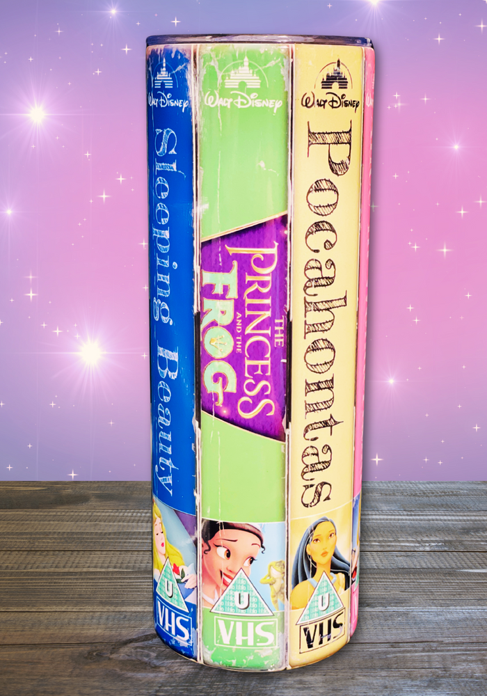 A 20 oz stainless steel insulated tumbler featuring a vibrant design with vintage Disney princess VHS covers, including Sleeping Beauty, The Princess and the Frog, and Pocahontas. Comes with a clear lid, metal straw, and straw cleaner, perfect for hot and cold drinks.