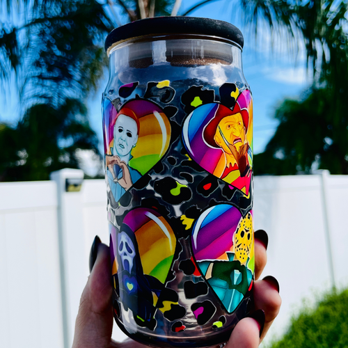 A 16 oz glass cup with a colorful design of rainbow hearts featuring horror movie icons like Michael Myers and Freddy Krueger, paired with a rainbow leopard bamboo lid and reusable glass straw.