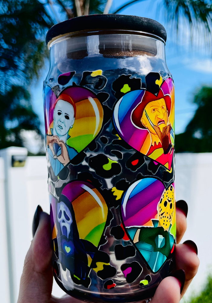 A 16 oz glass cup with a colorful design of rainbow hearts featuring horror movie icons like Michael Myers and Freddy Krueger, paired with a rainbow leopard bamboo lid and reusable glass straw.