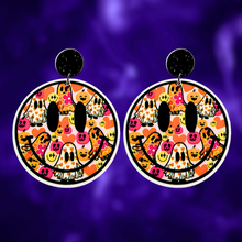 Load image into Gallery viewer, A purple background with earrings featuring a smiley face filled with colorful ghosts and flowers, perfect for a fun and lighthearted Halloween look
