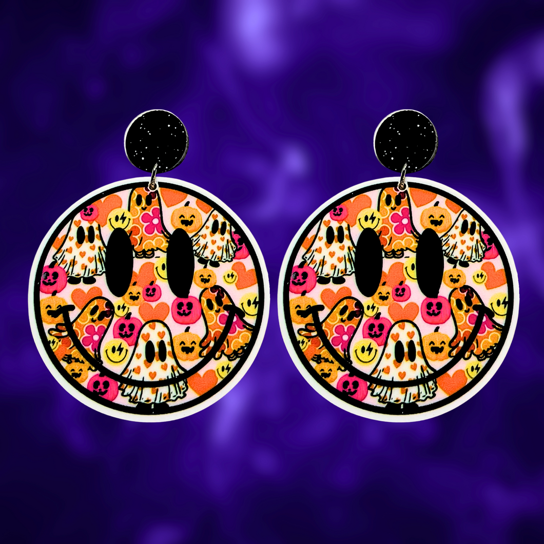 A purple background with earrings featuring a smiley face filled with colorful ghosts and flowers, perfect for a fun and lighthearted Halloween look