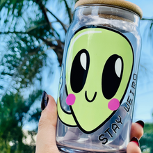 Load image into Gallery viewer, A 16 oz glass cup featuring a cute green alien design with the words &quot;Stay Weird,&quot; paired with a bamboo lid and reusable glass straw. Perfect for quirky drinkware lovers and iced coffee enthusiasts.
