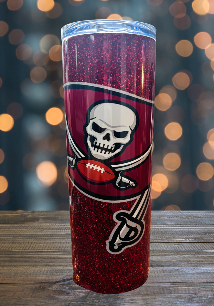 A 20 oz stainless steel insulated tumbler featuring a glittery red design with the Tampa Bay Buccaneers flag logo. Comes with a clear lid, metal straw, and straw cleaner, perfect for hot and cold drinks. Discounted due to a thin white seam on the back.