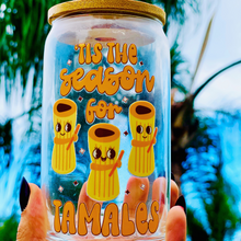 Load image into Gallery viewer, A 16 oz glass cup featuring a cute tamale-themed UVDTF wrap with the phrase “’Tis the Season for Tamales.” Includes a bamboo lid and reusable glass straw, perfect for cold drinks. BPA-free and handwash only.
