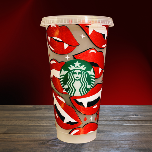 A 16 oz BPA-free Starbucks-compatible reusable cold cup featuring a glittery vinyl wrap with bold red vampire lips and fangs. The cup includes a clear lid and reusable straw, ideal for iced coffee lovers and fans of vampire-themed shows like True Blood and Twilight.