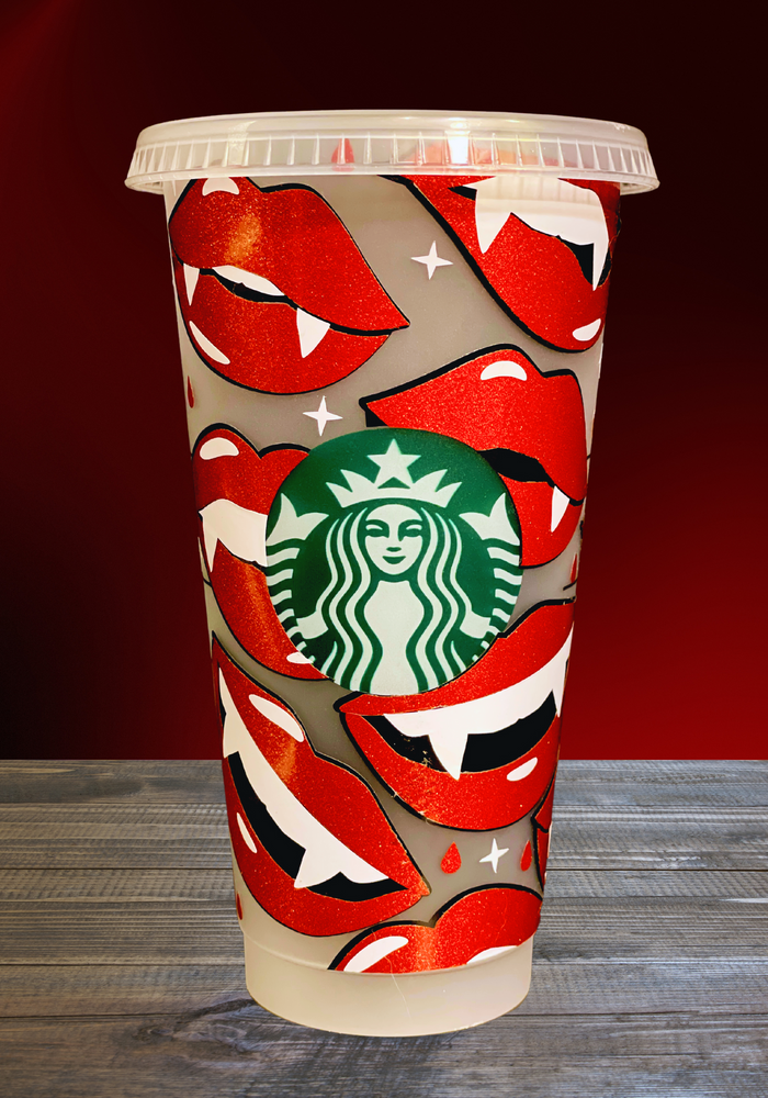 A 16 oz BPA-free Starbucks-compatible reusable cold cup featuring a glittery vinyl wrap with bold red vampire lips and fangs. The cup includes a clear lid and reusable straw, ideal for iced coffee lovers and fans of vampire-themed shows like True Blood and Twilight.