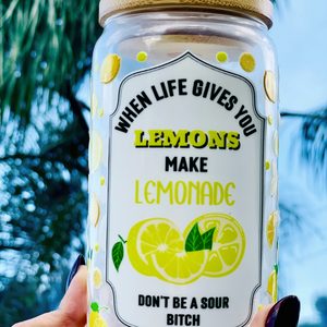 16 oz BPA-free glass cup with a vibrant lemon design and cheeky quote: 'When life gives you lemons, make lemonade, don’t be a sour bitch.' Includes a bamboo lid and reusable glass straw.