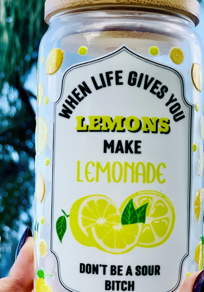 16 oz BPA-free glass cup with a vibrant lemon design and cheeky quote: 'When life gives you lemons, make lemonade, don’t be a sour bitch.' Includes a bamboo lid and reusable glass straw.
