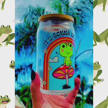 Load and play video in Gallery viewer, A 16 oz glass cup featuring a colorful UVDTF wrap with a smiling frog on a mushroom under a rainbow and the text “It’s Gonna Be Okay.” Comes with a bamboo lid and reusable glass straw. BPA-free and handwash only.
